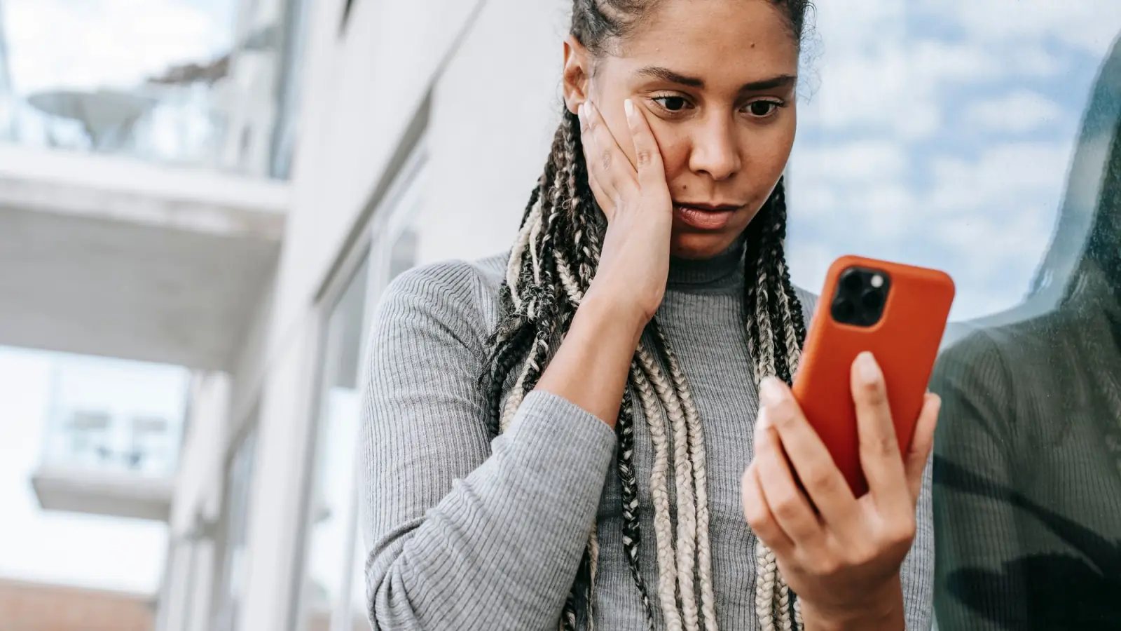 Mulher preocupada, com a mão no rosto, olha para a tela do celular